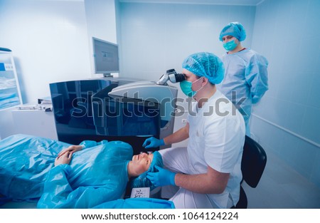 Laser vision correction. A patient and team of surgeons in the operating room during ophthalmic surgery. Eyelid speculum. Lasik treatment. Patient under sterile cover Royalty-Free Stock Photo #1064124224