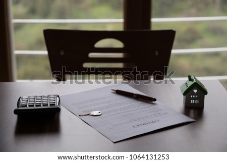 Real estate contract ,calculator, key, house and pen on the wooden table in front of the window.