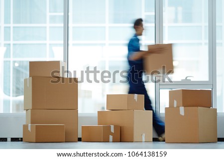 Blurred motion of contemporary worker with packed box walking to new office while delivering it to client Royalty-Free Stock Photo #1064138159