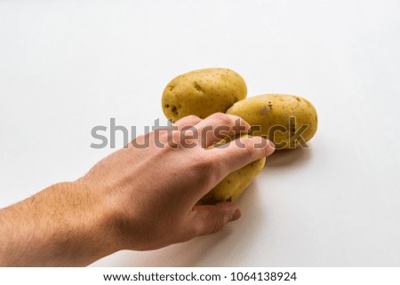 Left hand holding a potato coming from bottom left side of the picture, two potatoes on white background and smooth shadow
