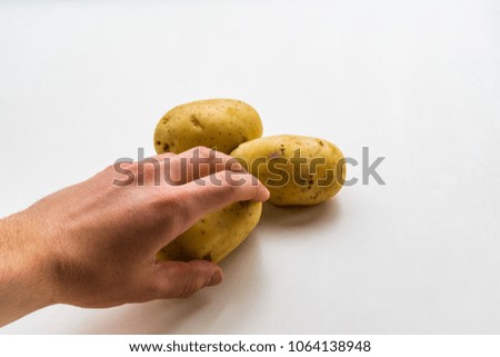 Left hand holding a potato coming from bottom left side of the picture, two potatoes on white background and smooth shadow