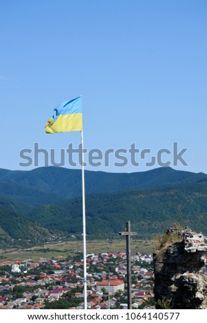 Ukraine flag and christian cross with panorama of Khust city background. View from ruin of old castle. Landscape, Zakarpattia Oblast. Ukraine.