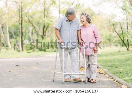 Happy loving Asian senior couple talking a walk with walker in the park Royalty-Free Stock Photo #1064160137