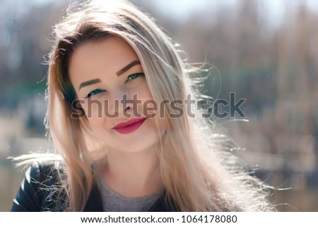 Outdoors portrait of beautiful young brunette girl. Woman smiling happy on sunny summer or spring day outside on city background. Close-up portrait in a golden hour. Selective focus.