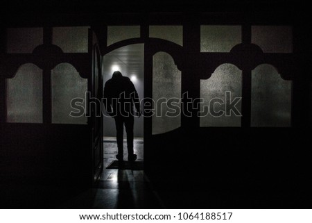 Silhouette of an unknown shadow figure on a door through a closed glass door. The silhouette of a human in front of a window at night. Scary scene halloween concept of blurred silhouette of maniac.
