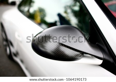 Close-up view of a carbon fiber side mirror on a white car with a blurry background.
