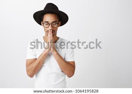 Keep calm and believe in miracle. Portrait of focused serious african-american in stylish eyewear and black hat, holding hands in pray over mouth, closing eyes while praying or making wish