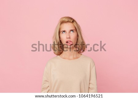 Bored to death! Young blonde female, feels drearily and looks above, shows her tongue with disgust. Isolated over pink background
