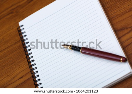 Fountain pen or ink pen with notebook paper on wooden working table with copy space, office desk concept idea.