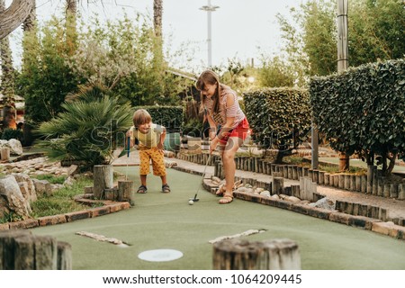 Group of two funny kids playing mini golf, children enjoying summer vacation Royalty-Free Stock Photo #1064209445