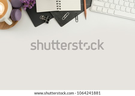 Flat lay, top view office table desk. Workspace with blank note book, keyboard, macaroon, office supplies, eyeglass and coffee cup on white background.
