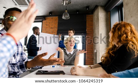 cheerful young teacher with raised hands talking with her multi-ethnic students