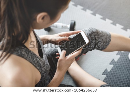 Young asian sportswoman sitting and using smartphone in gym