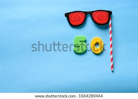 50 celebrating yellow number with sunglasses cute paper mask on straw stick. Fifty Modern alphabet digits on blue background. 50 th birthday party anniversary card.Flat lay, top view.Copy space.