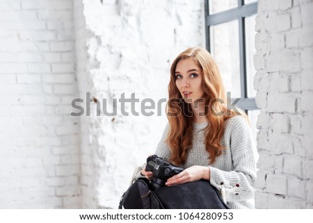Young female photographer with camera sitting near window in photo studio