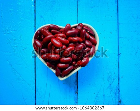Red beans in bowl shape heart on isolated blue background, concept healthy