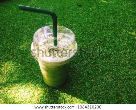 A glass of green tea place on green grass background with copy space for your text and design. Concept be used for present about menu in coffee shop and coffee shop business. Blur picture.