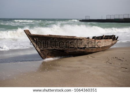large waves during a storm on the sea cover a small old wooden boat