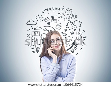 Dreamy young woman with brown hair wearing a blue shirt and business suit pants is looking upwards and thinking. A gray wall background with a start up sketch Creative thinking concept