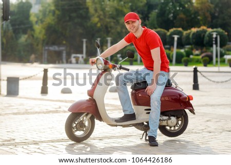 Young man posing with a bike on the city street. Cheerful deliverer is having a rest after work.