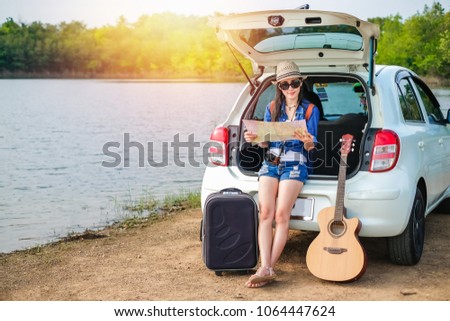 woman of traveler sitting on hatchback of car and looking at the map for find destination near the lake during holiday.Young lady tourist enjoying on vacation. 