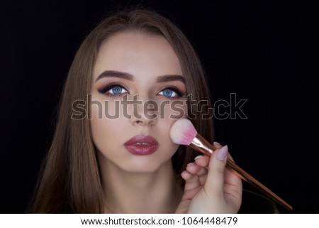 A girl on a black background holds a make-up brush. Professional makeup. We do make-up.