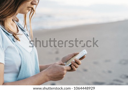 young pretty hipster girl using white smart phone at the beach/ space for your text