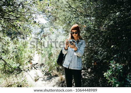 young beautiful woman taking picture with a vintage camera during hiking in the mountains / pretty girl in a red beanie making photo in the nature mockup space for text