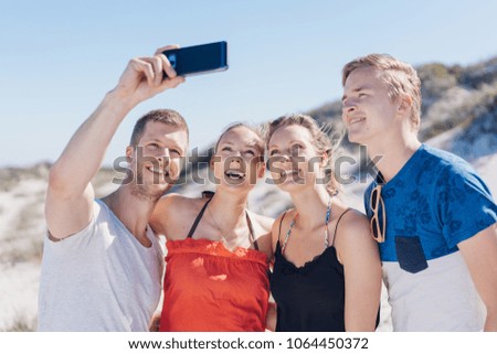 Happy laughing friends taking a selfie on a beach as they pose amongst the coastal sand dunes joking and smiling