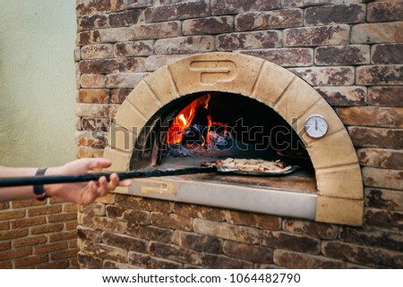 cook puts pizza with shovel in a hot stove