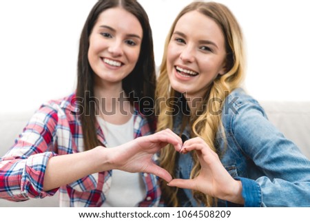 The two happy girls show the heart symbol on the white background