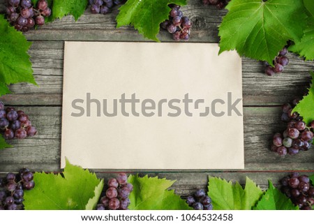Vine with grapes and leaves around on vintage rustic wooden table. Old paper template in centre of background. Top view