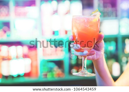 selective soft focus with dramatic lighting of A woman hand holding glass beverage alcohol drinking cocktail fruit juice mix. background bar colorful light
