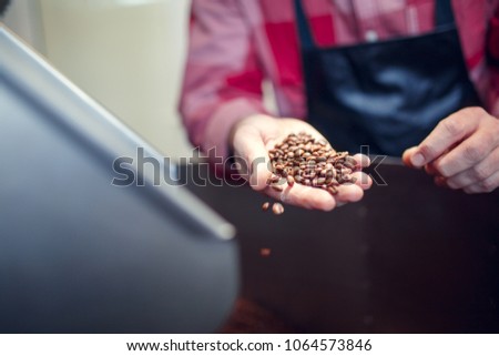 Photo of young businessman holding roasted coffee beans near industrial coffee grinder