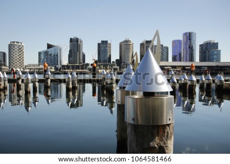 A silver sculpture in Docklands with reflection of building on the water in the background