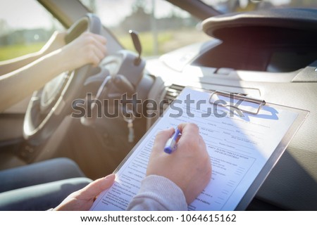 Examiner filling in driver's license road test form sitting with her student inside a car Royalty-Free Stock Photo #1064615162