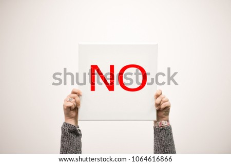 Female hands holding up a square white sign with the word NO in red font 