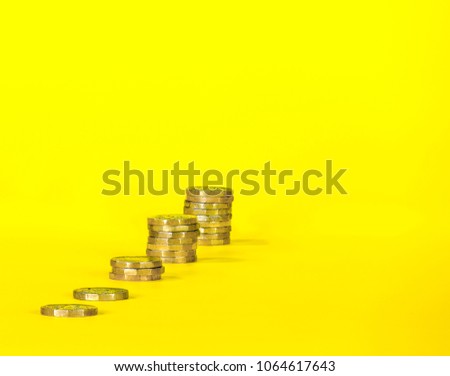 Gold Coins on a Bright Yellow Background. Stacked and growing bigger into the image. Royalty-Free Stock Photo #1064617643