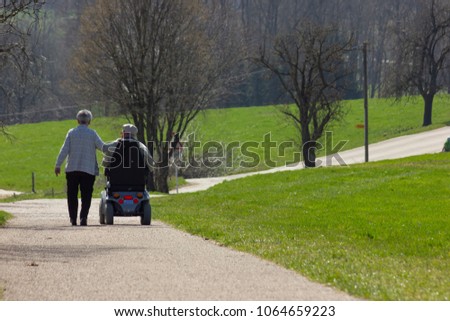 senior couple with motordriven wheelchair on blue sky sunny holiday at eastern springtime in south germany Royalty-Free Stock Photo #1064659223