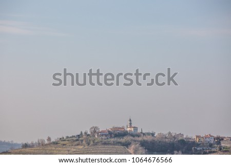 Panoramic view of a rural village with church on the top of the hill in the alps near Dobrovo, Slovenia. Place for text in tender blue sky background.
