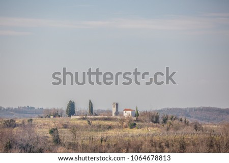Panoramic view of a rural village with cemetry on the top of the hill in the alps near Dobrovo, Slovenia. Place for text on tender blue sky background
