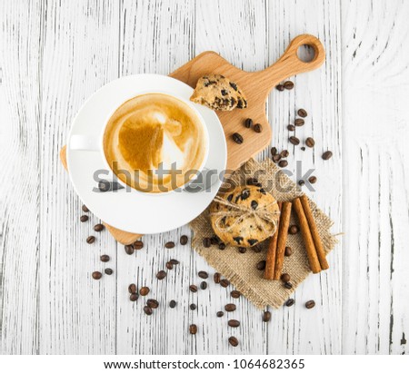 Coffee cup, chocolate cookies, pieces of cinnamon and scattered coffee beans on a white vintage wooden table. Top view. Coffee break. 