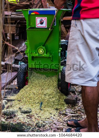 a man use chopper branch machine for change wood to saw dust for make natural fertiliser. on green machine have sign don't insert hand here.