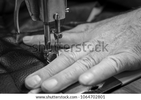 Sewing process of the leather belt. old Man's hands behind sewing. Leather workshop. textile vintage sewing industrial, black and white, b&w