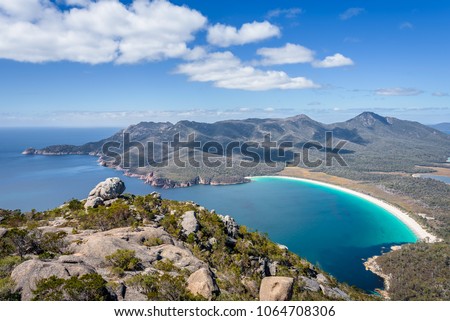 Relaxing amazing mountain viewpoint stunning view to Wineglass Bay sandy beach blue water and enjoyng warm sunny blue sky after hiking on top, Freycinet National Park, Mount Amos, Tasmania, Australia Royalty-Free Stock Photo #1064708306