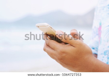 Close up of a man hand holding using mobile smart phone outdoor cellphone on the beach and Mountain. with filter Tones vintage effect ,Warm tones.