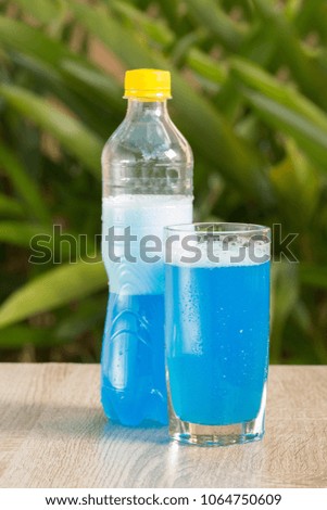 A glass with a blue drink stands on a table on a green background