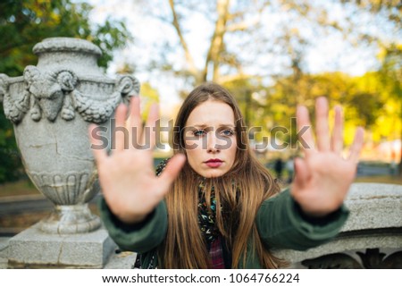 Attractive young woman in park is displeased and making a stop sign with her hands
