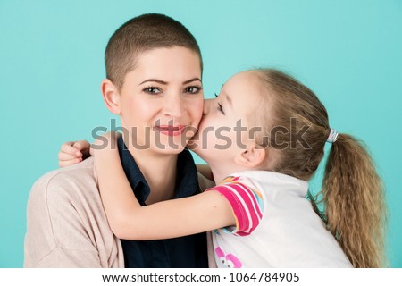 Young girl kissing mother, young cancer patient, on the cheek. Cancer and family support concept.