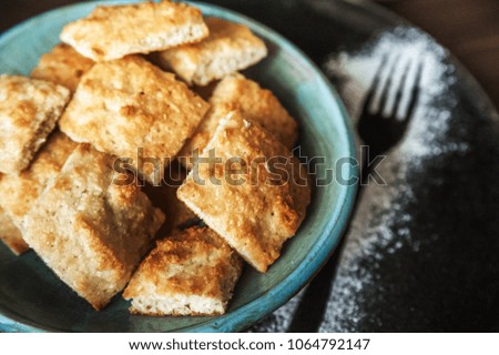 Appetizing picture of food, blue plate with a square home cookie on a background of a dark wooden table. Cookie structure. Sugar powder sprinkled with a fork